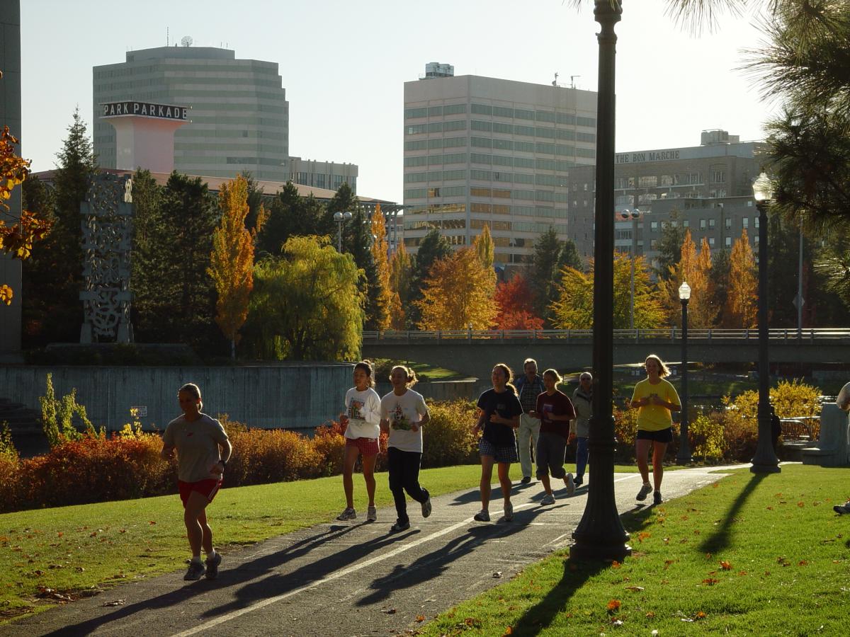 Runners along an urban trail surrounded by trees and the cityscape.